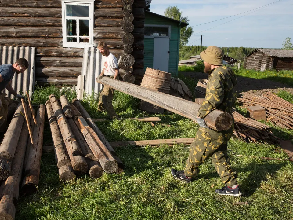 Двое несут бревно у старого сруба